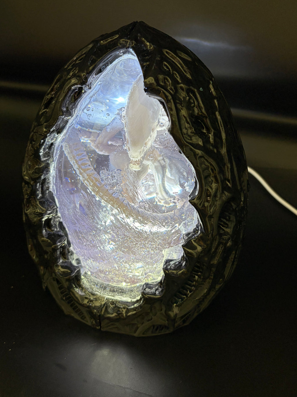 Above-left angle view of the Shardlurker Specimen Night Light with the translucent blue resin egg glowing while the light is on