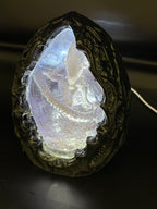 Above-left angle view of the Shardlurker Specimen Night Light with the translucent blue resin egg glowing while the light is on