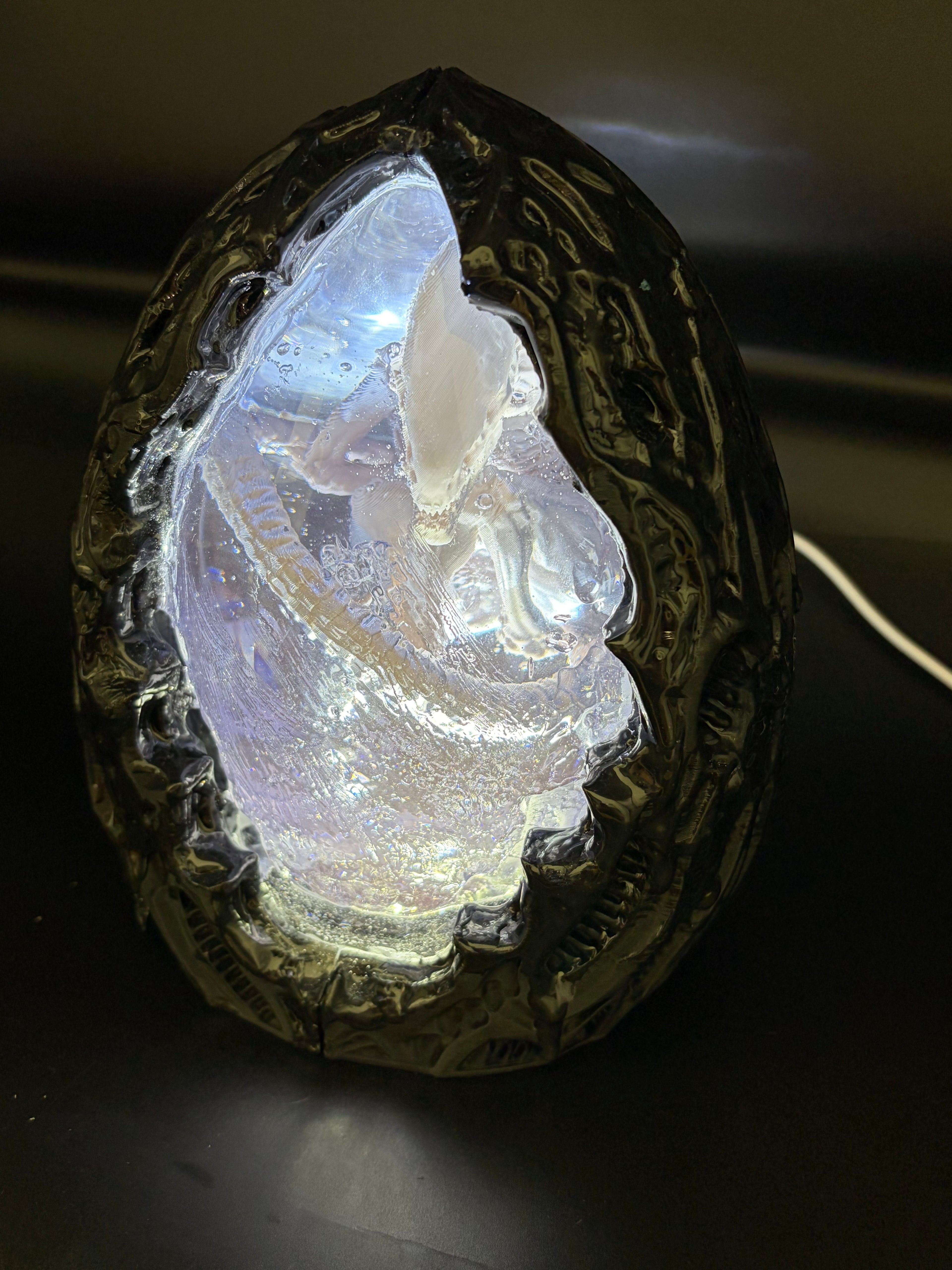 Above-left angle view of the Shardlurker Specimen Night Light with the translucent blue resin egg glowing while the light is on