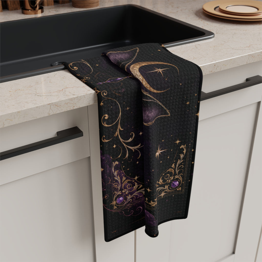 Vespertine Gothic Moon Bat microfiber tea towel draped beside a kitchen sink, showing black fabric with purple and gold celestial artwork