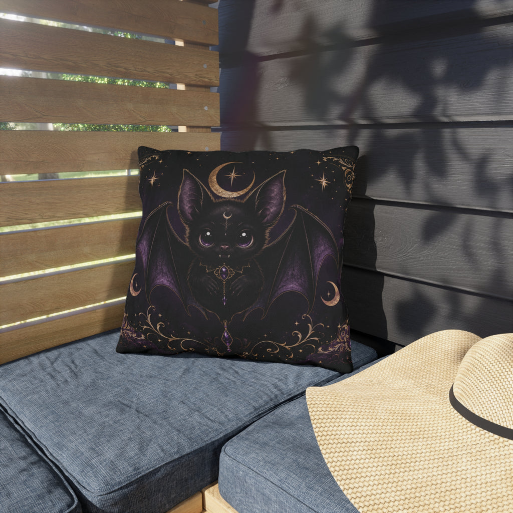 Vespertine Gothic Moon Bat outdoor throw pillow displayed on a patio chair, featuring a black bat, crescent moon, stars, and purple celestial details