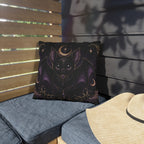 Vespertine Gothic Moon Bat outdoor throw pillow displayed on a patio chair, featuring a black bat, crescent moon, stars, and purple celestial details
