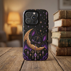 Vespertine Gothic Moon Bat phone case displayed beside vintage books, featuring a black bat on a gold crescent moon with purple crystals and starry celestial details