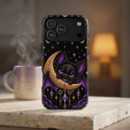 Vespertine Gothic Moon Bat phone case displayed beside a mug in a cozy setting, featuring a black bat on a gold crescent moon with purple crystals and starry celestial details